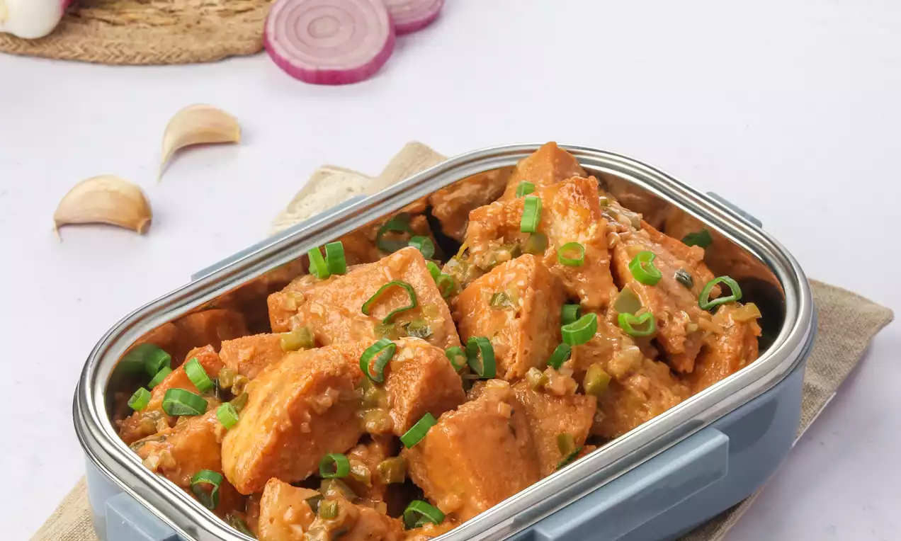 Golden-brown fried idli cubes coated in glossy orange Manchurian sauce, garnished with fresh green onion, served in a blue dish