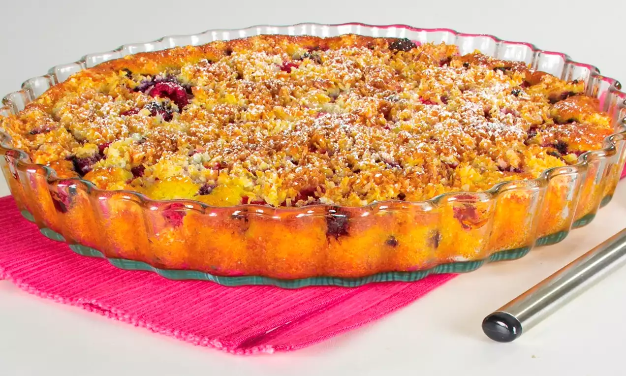 Pyöreä, kirkkaassa lasivuoassa oleva marjapiirakka, jonka kultainen murupinta on kevyesti tomusokeroitu ja marjojen sävyt pilkistävät joukosta