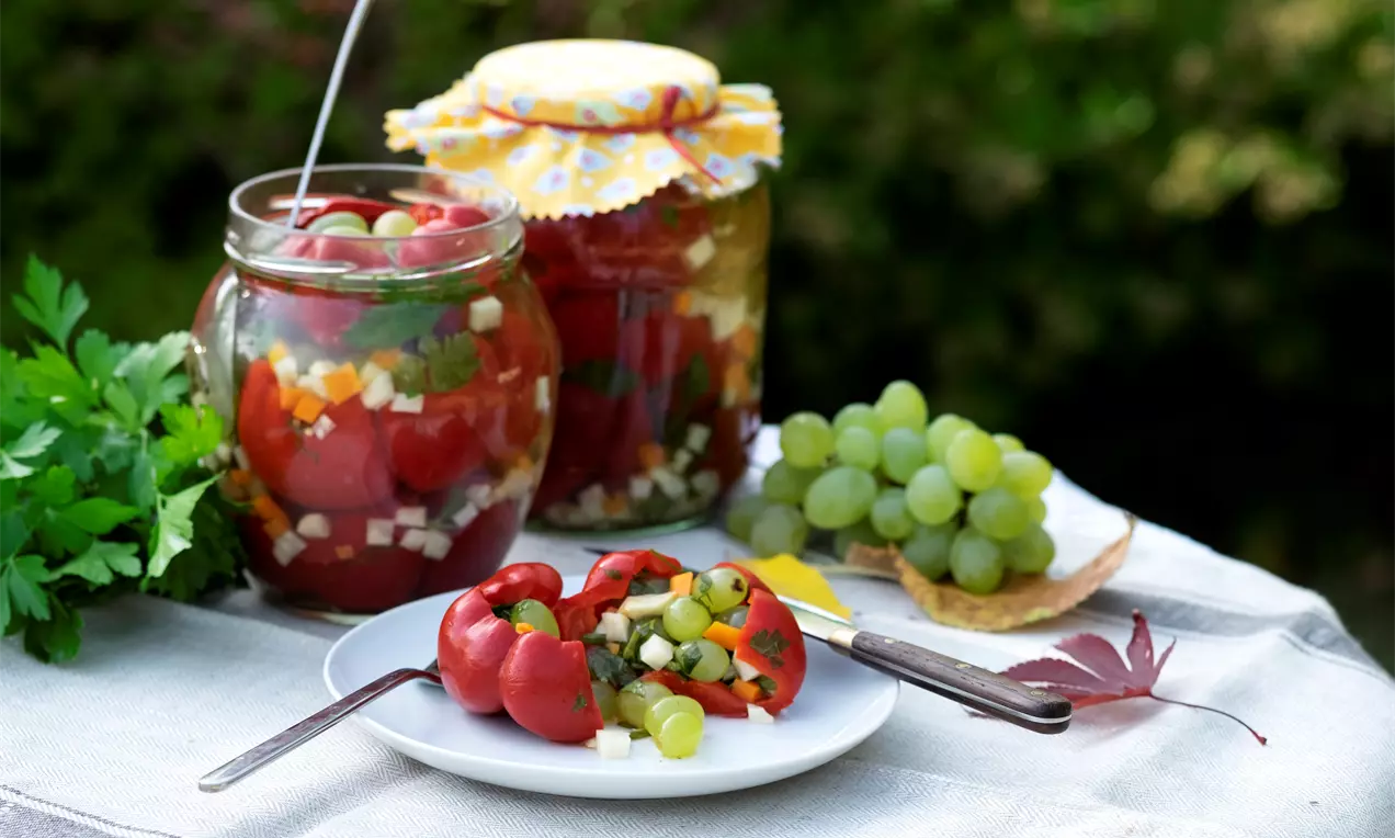 Червени камби, пълнени със зеленчуци и бледозелено грозде, поднесени върху бяла чиния, декорирана с есенни листа и магданоз