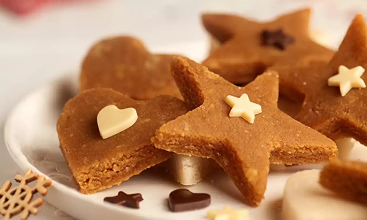 Figuras de turrón de yema color dorado con textura suave, formas de estrella y corazón decoradas con pequeños adornos de chocolate blanco y negro sobre un plato blanco