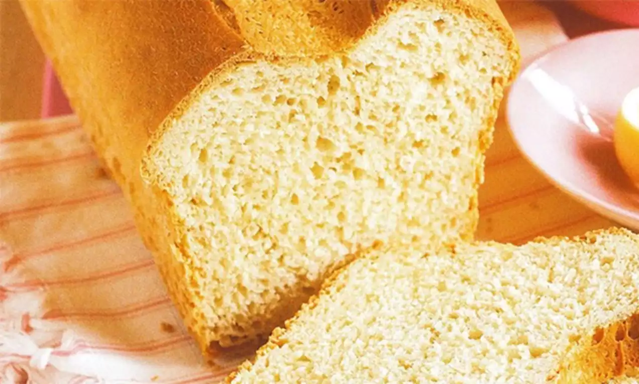 Witbrood met een goudbruine korst en een luchtige, zachte binnenkant, deels gesneden, op een pastelroze doek en een bord met boter