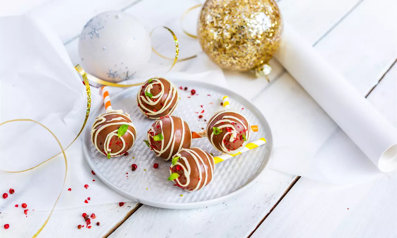 Кръгли бонбони от гладък кафяв шоколад с бели линии и зелени листенца върху релефна бяла чиния, заобиколени от златна гирлянда и орнаменти