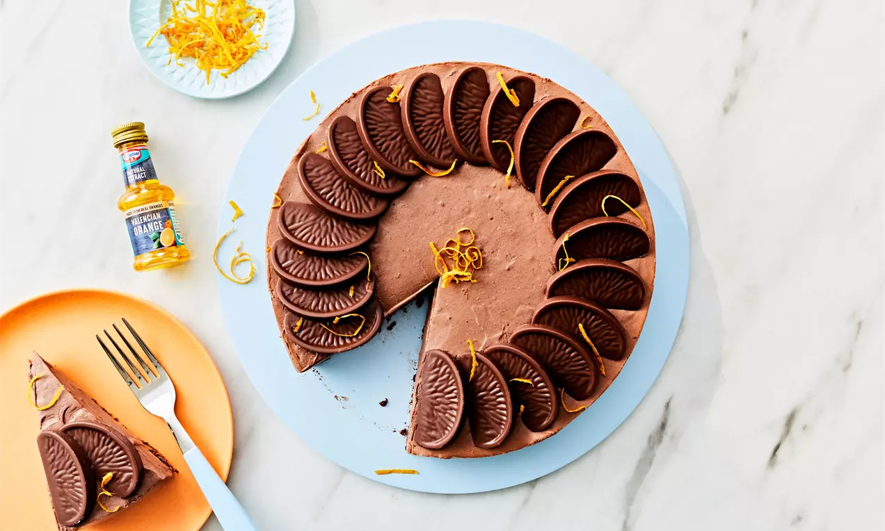 Round chocolate cheesecake topped with neatly arranged dark chocolate biscuits and thin orange zest curls on a pale blue plate