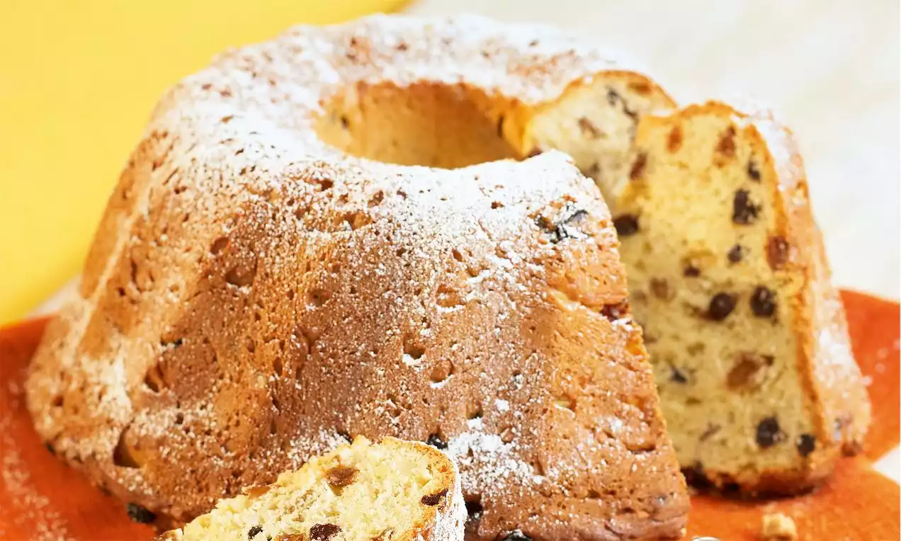 Kouglof doré aux raisins secs en spirale, saupoudré de sucre glace, avec des tranches moelleuses sur un plat orangé