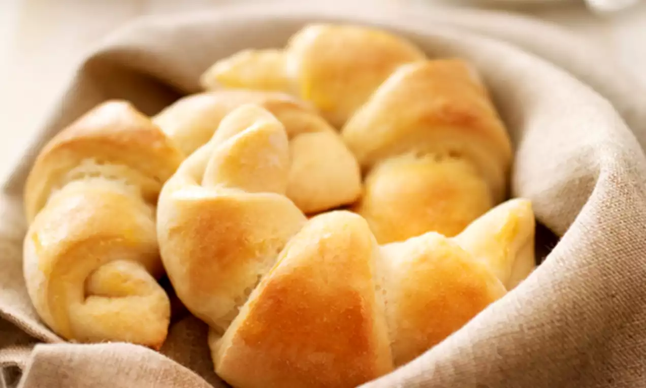Goldgelb gebackene, leicht gebogene Quarkhörnchen mit zarter, glatter Oberfläche in einem rustikalen Leinentuch auf einem Tisch arrangiert