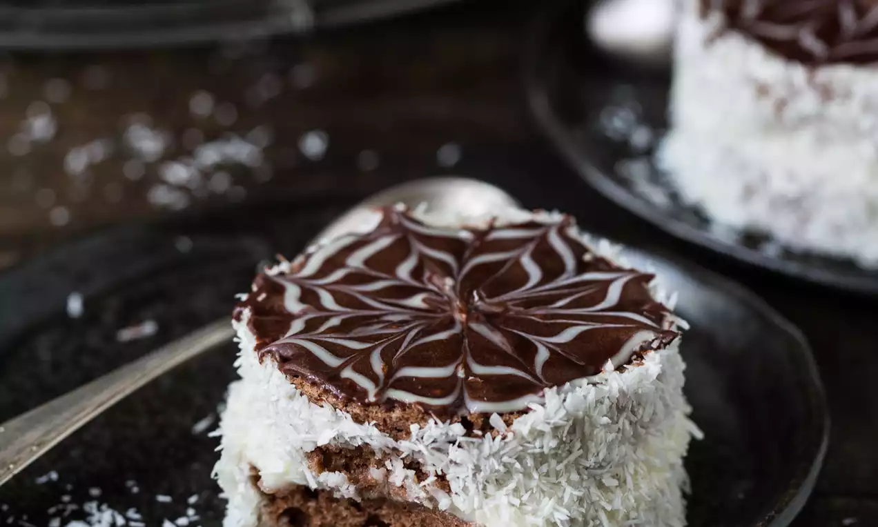 Ruska kapa s čokoladnim biskvitom, bogatim filom, obložena kokosom i ukrašena tamnom čokoladom sa svijetlim uzorkom na crnom tanjiru