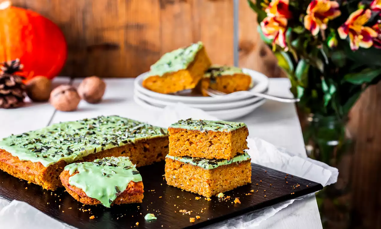 Bal kabaklı kek ince kesilmiş kare dilimlerle sunulmuş, yeşil çikolata kaplamasıyla parlıyor ve üzerine serpiştirilmiş parçalar bulunuyor