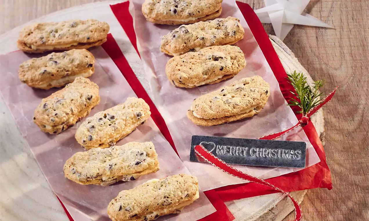 Světlé sněhové tyčinky s karamelovým nádechem, křupavou texturou a kousky čokolády na pergamenu, dekorované červenou stuhou a větvičkou jedle