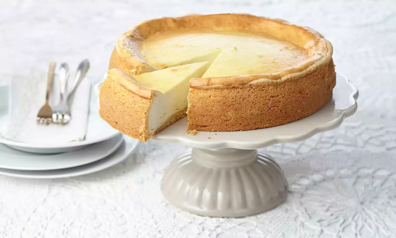 Käsekuchen mit goldbrauner Oberfläche und cremigem, hellem Innenleben auf knusprigem Mürbeteig, serviert auf weißem Teller mit Gabel