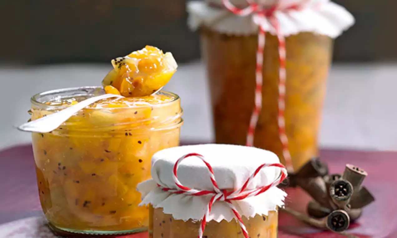 Goldorange Kaki-Orangen-Konfitüre mit feinen Ingwerstückchen, in Gläsern mit Stoffdeckeln und rotem Band auf hellem Untergrund drapiert