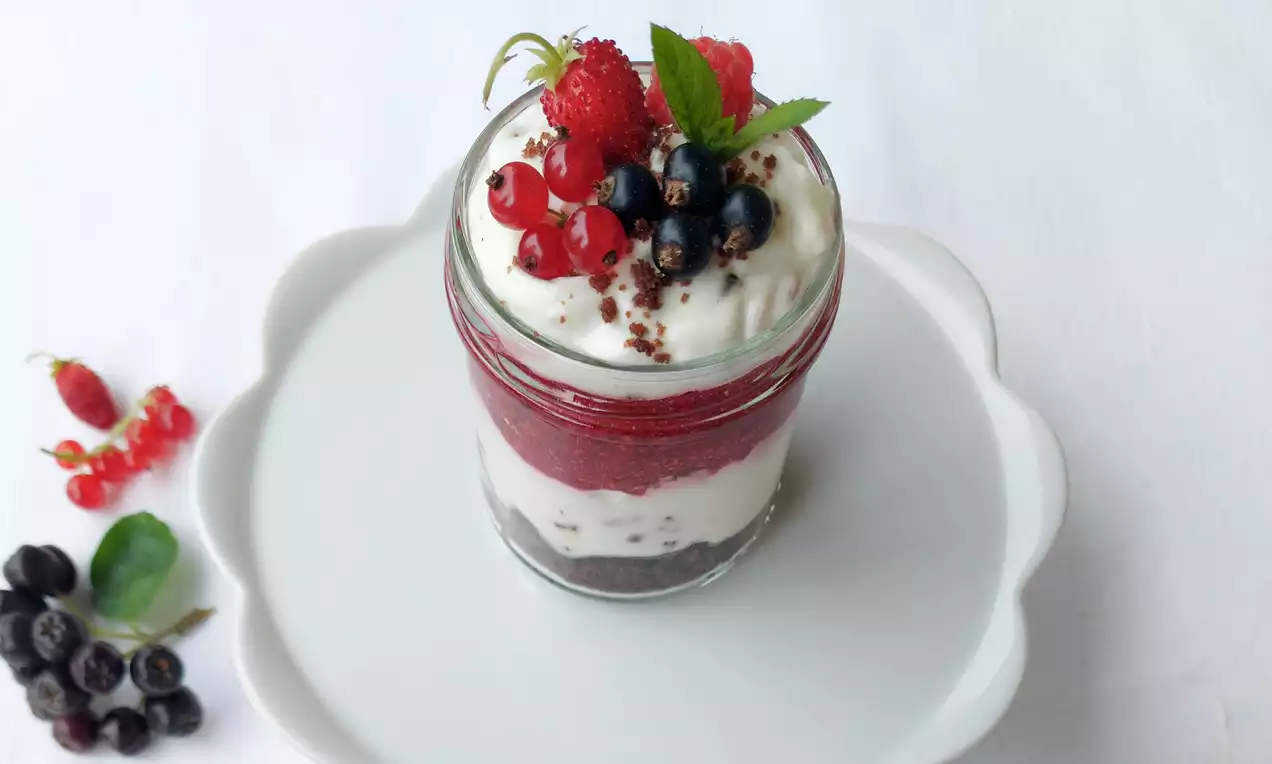 Krtkův dort ve sklenici s tmavou sušenkovou základnou, světlým krémem, červenou vrstvou ovocného pyré, lesním ovocem a lístky máty