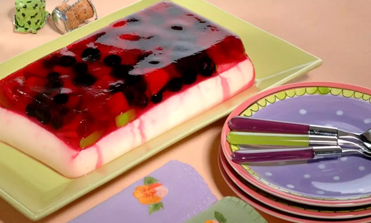 Roomwitte pudding met geelgroene en rode ondertonen onderdoorzichtige rode jelly met fruitstukjes op een lichtgroene schaal