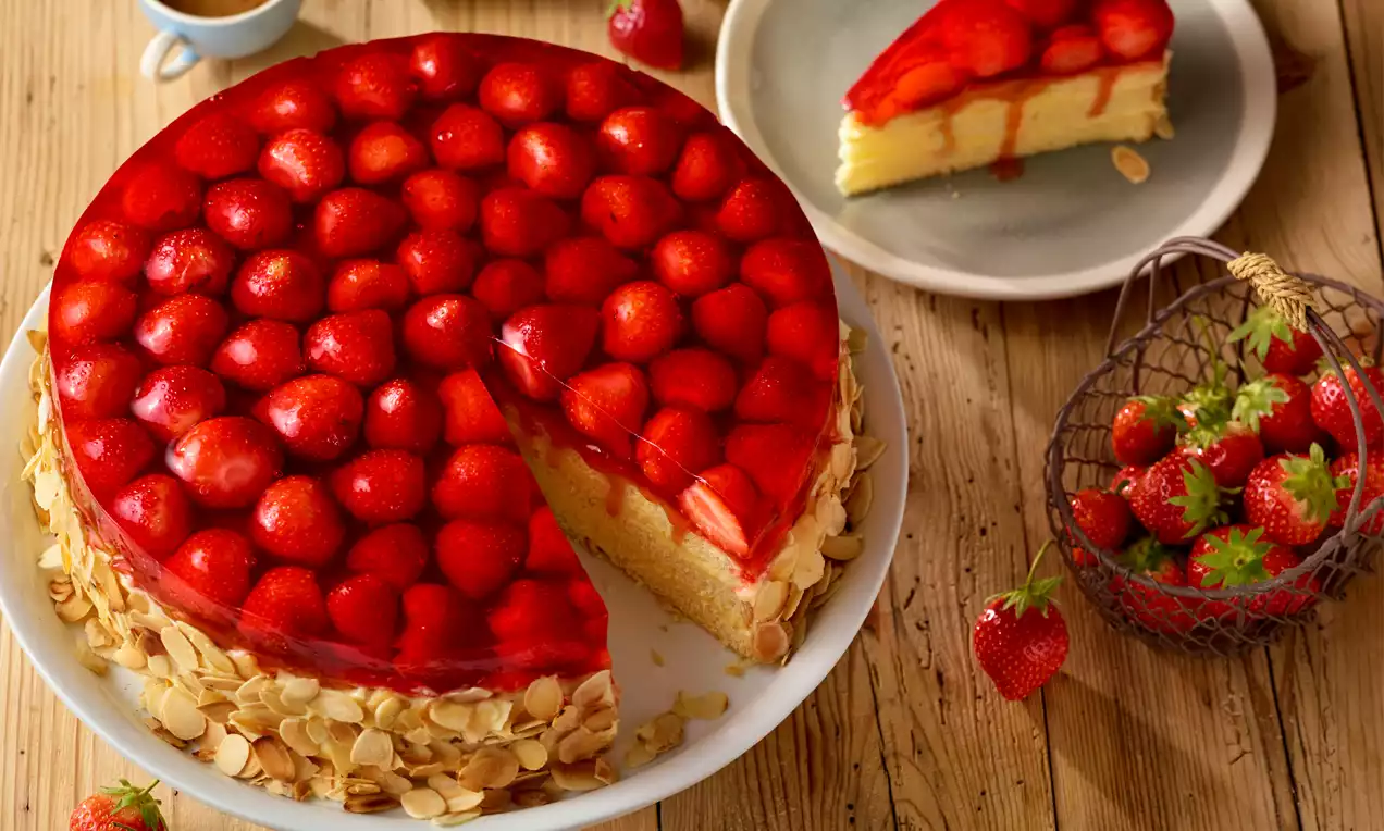 Klassische Erdbeertorte mit glänzenden roten Erdbeeren, roter Geleeschicht, goldgelbem Tortenboden und gerösteten Mandelblättchen auf weißer Platte