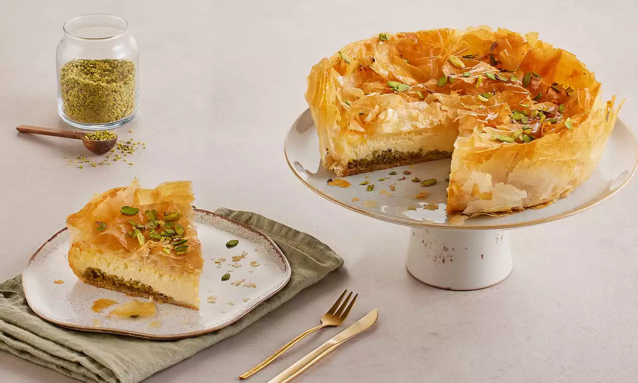Kat kat çıtır hamurla çevrelenmiş kremalı cheesecake dolgusu, ince kıyılmış antep fıstığı süslemesi ve yanında porsiyon tabağı
