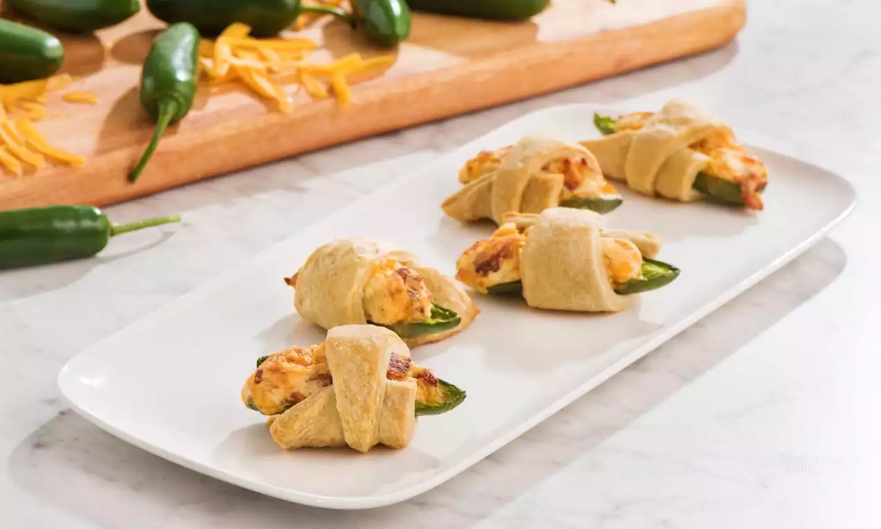 Jalapeños verts garnis de fromage doré, enroulés dans une pâte croustillante cuite, disposés par rangée sur une assiette blanche