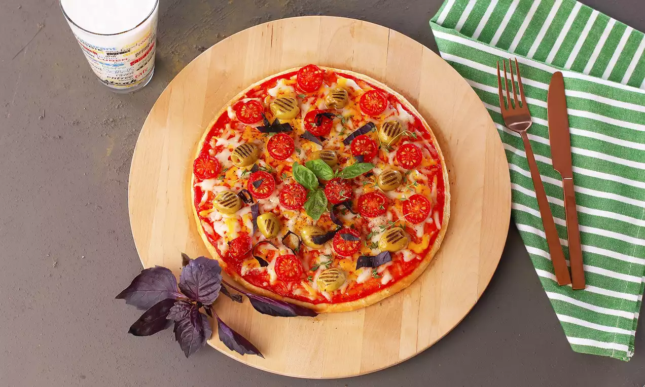 Ahşap servis tahtası üzerinde ince hamurlu, üzeri domates dilimleri, zeytinler, dört çeşit peynir ve taze fesleğen yapraklarıyla süslenmiş pizza