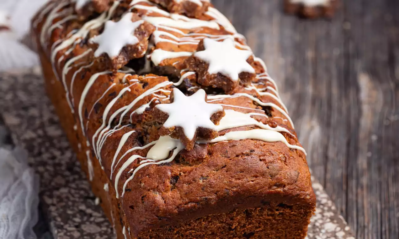 Božični bananin kruh tople rjave barve, preliven z belim sladkornim prelivom in okrašen z belimi zvezdicami na rustikalni podlagi