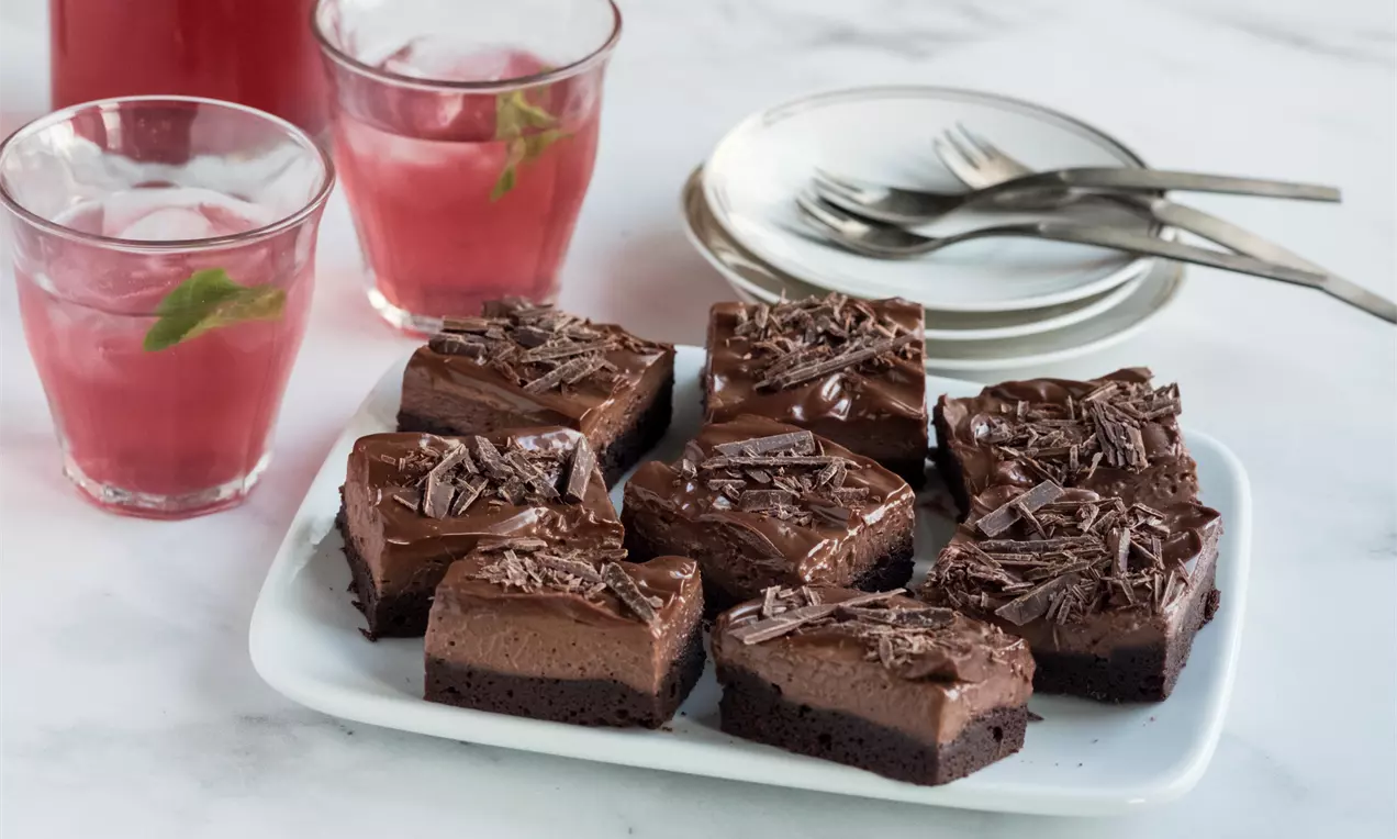 Шоколадови петифури с правоъгълна форма и тъмнокафяв слой с лъскава глазура, поръсени с шоколадови стърготини върху бяла чиния