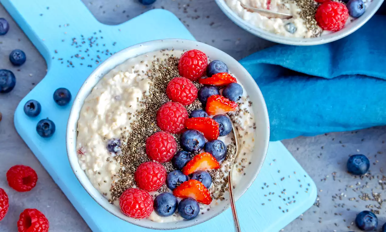 Cremiges, helles Vanille-Porridge in einer Schale, belegt mit roten Himbeeren, blauen Heidelbeeren, frischen Erdbeeren und Chiasamen