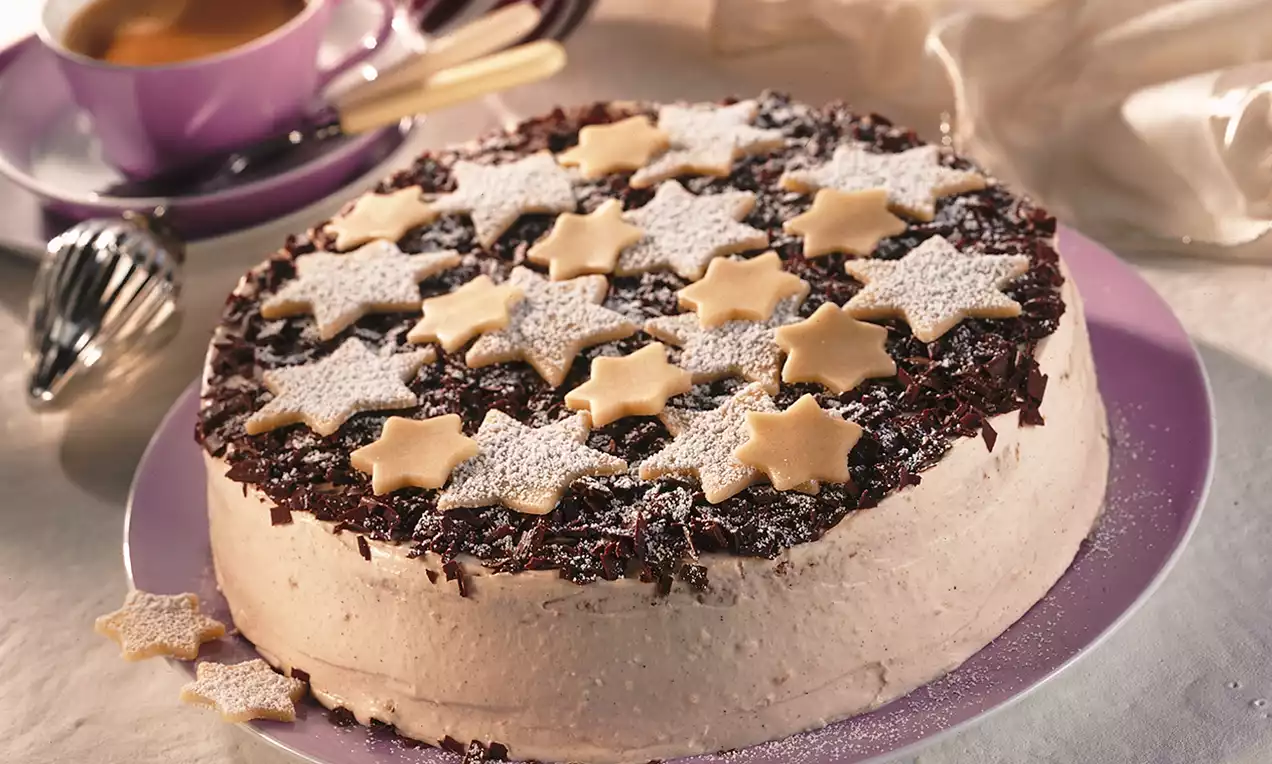 Okrugla torta s blagom bež kremom, tamnim čokoladnim strugotinama i ukrasnim zvjezdicama od tijesta posutim šećerom na ljubičastom tanjiru