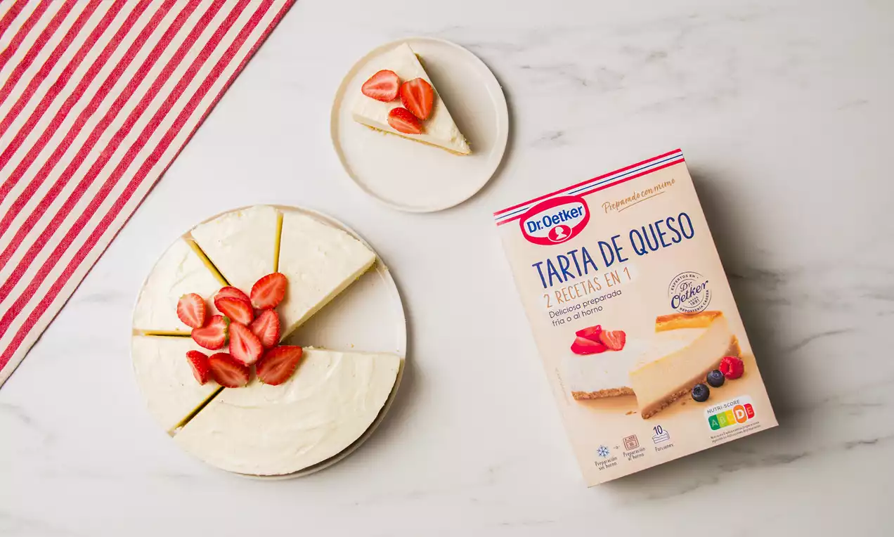 Tarta de queso fría con textura cremosa y superficie lisa decorada con fresas cortadas sobre plato blanco en fondo de mármol