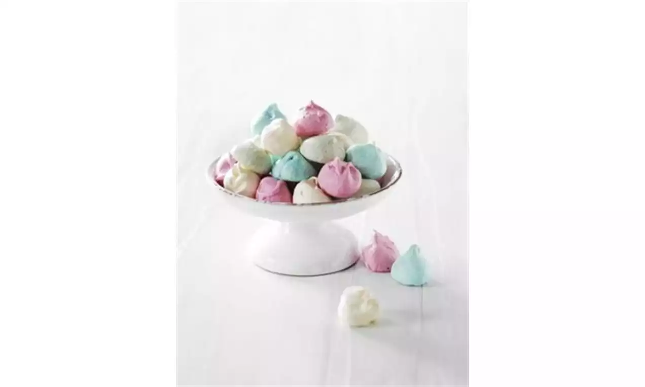 Små marengstopper i pastellfargene rosa, blå og hvit, stablet på et hvitt kakefat med noen få plassert på et lyst underlag