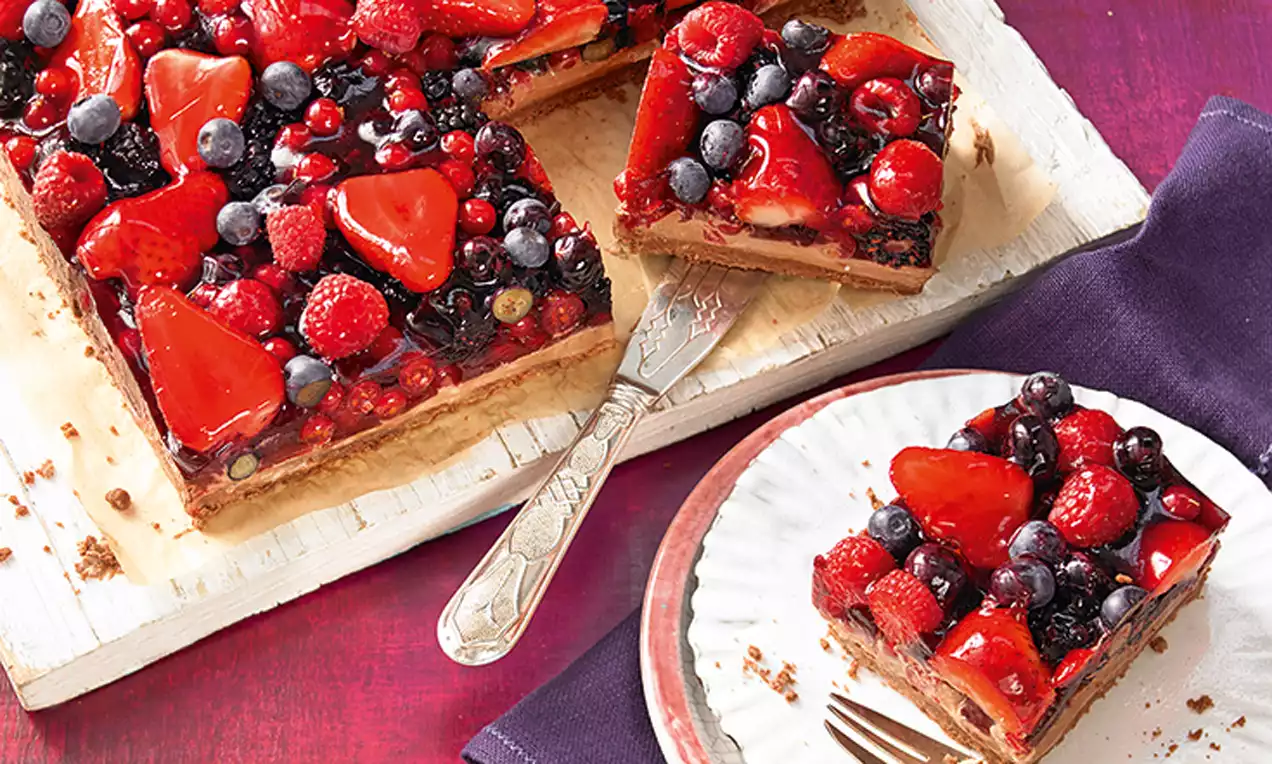 Suklainen marja-mascarponetorttu, jossa kiiltävä punamarjainen täyte tasaisesti levitettynä, tarjoiltuna puualustalla ja kynttilänpunaisella taustalla