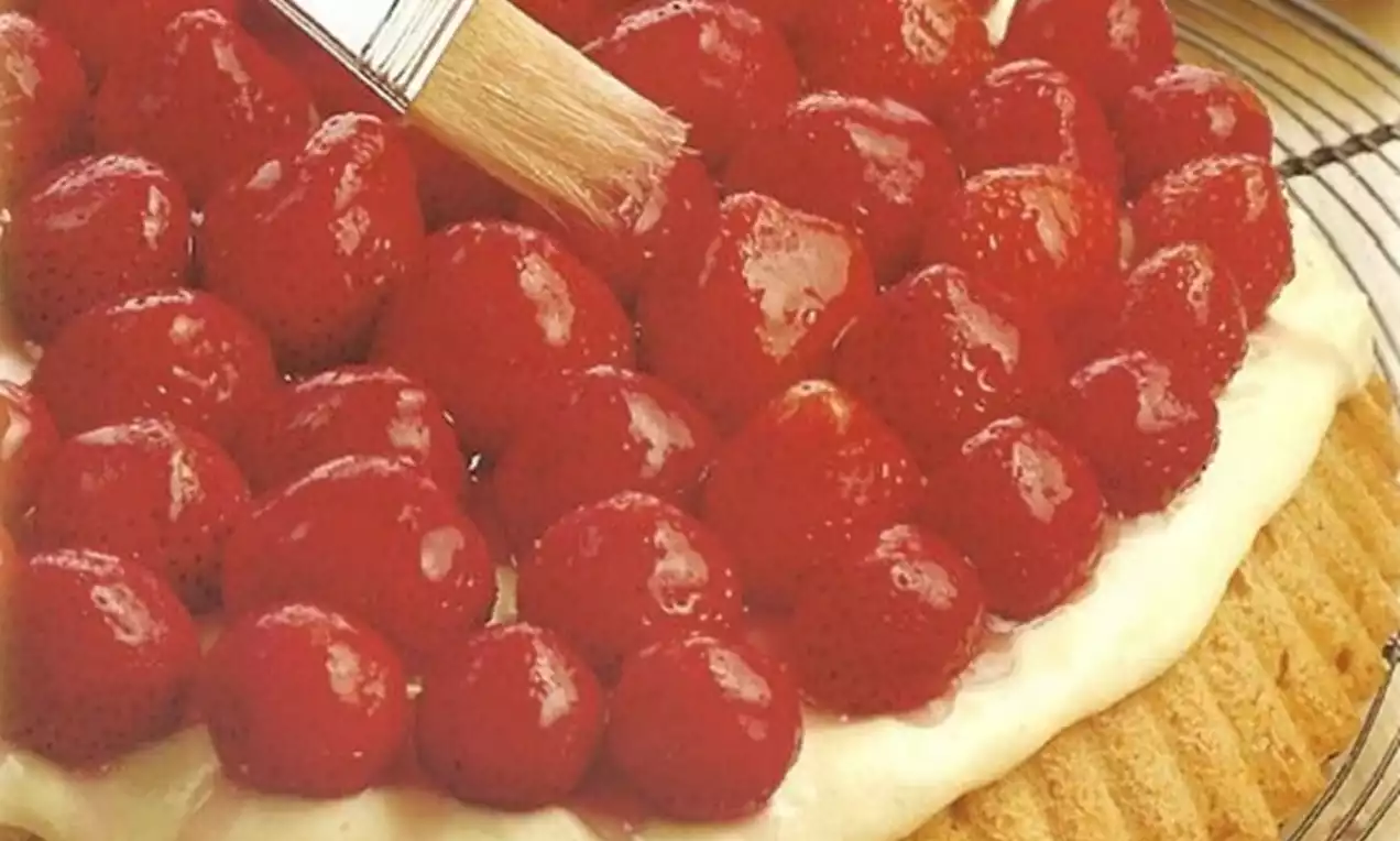 Aardbeientaart met een goudgele geribbelde koekbodem, een laag romige witte vulling en glanzende rode aardbeien, gepresenteerd op een glazen schaal