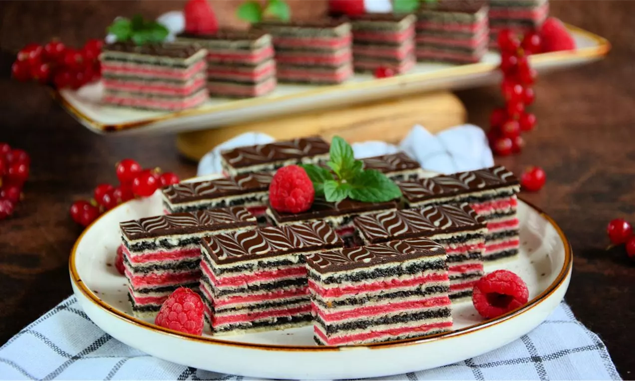 Čokoladne rozen kocke sa slojevima maka i malina, s mermernim šarama na vrhu, ukrašene svežim malinama i listićem mente na tanjiru