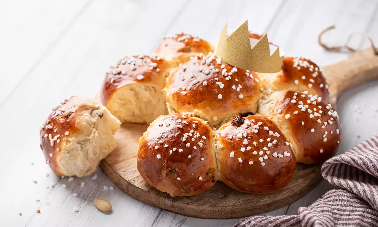 Couronne dorée en brioche moelleuse, brillante, garnie de sucre perlé, posée sur une planche en bois avec une petite couronne en papier