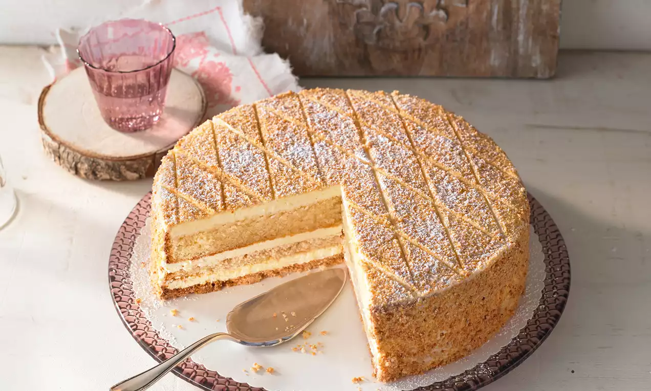 Zuger Kirschtorte mit goldbrauner Oberfläche, feinem Gittermuster, Puderzucker, heller Cremefüllung und Nussrand auf einer Platte