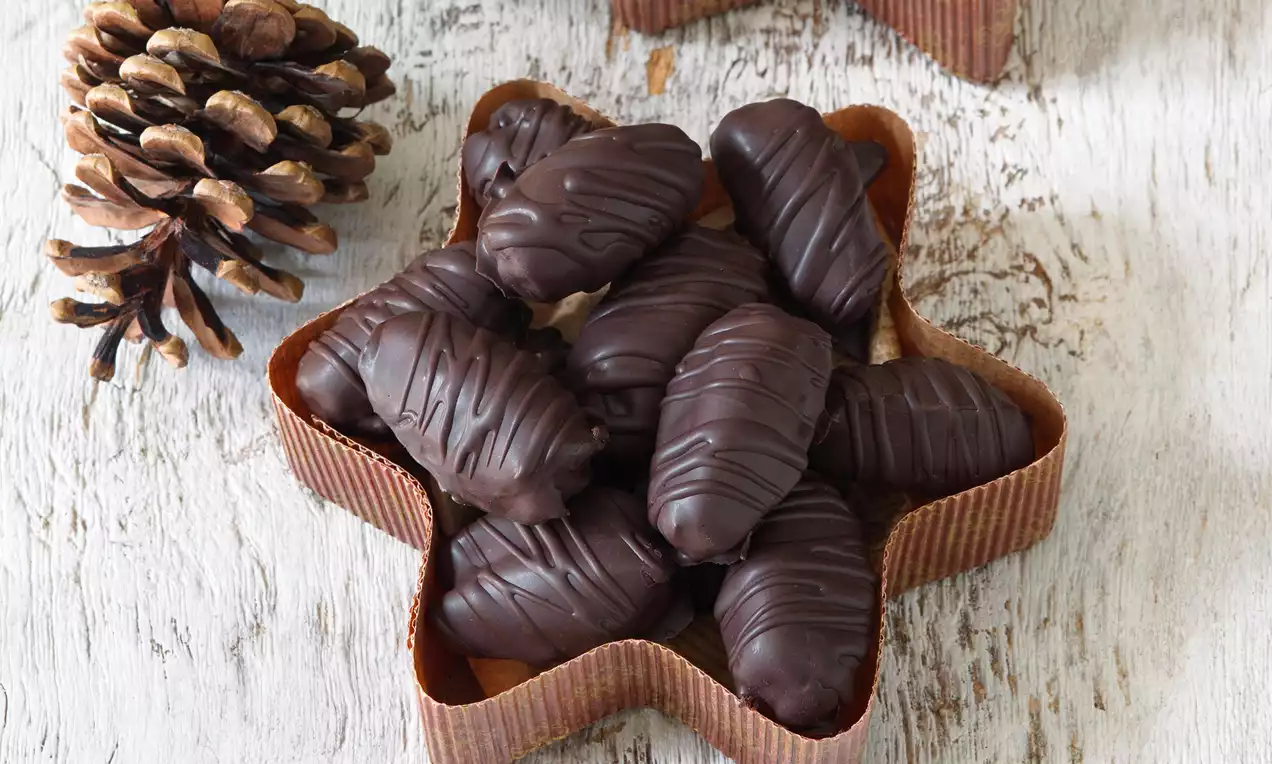 Datlové konfety tmavě hnědé s jemně lesklým čokoládovým povrchem zdobené tenkými linkami, uspořádané do hvězdicové misky na světlém dřevě