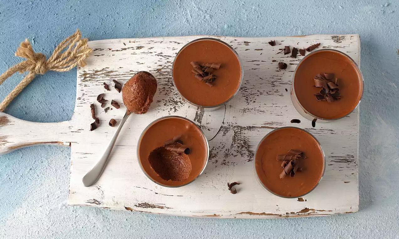 Dört adet küçük bardakta kremsi çikolatalı mousse, üzerinde çikolata parçalarıyla beyaz ahşap bir sunum tahtasında düzenlenmiş