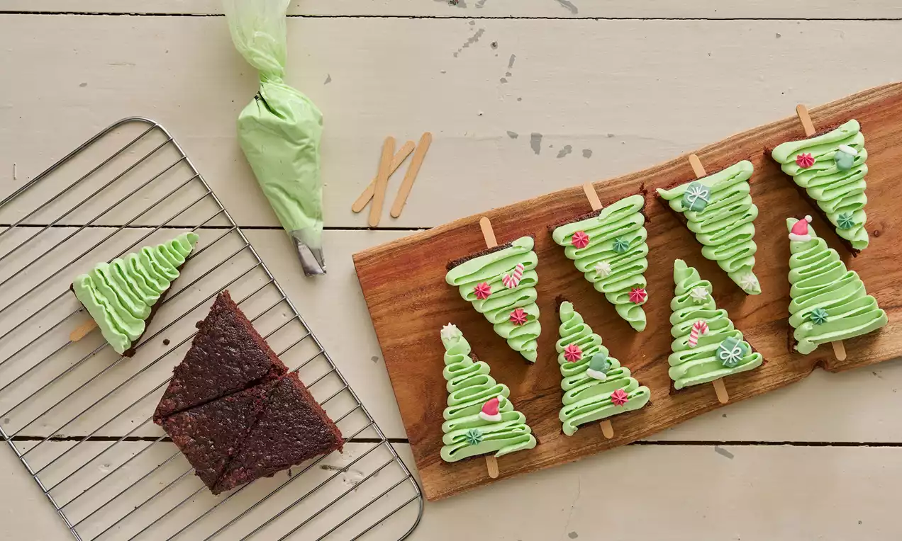 Brownie-treformede stykker med lysegrønn glasur og dekorative røde og hvite detaljer, montert på ispinner på en trefjøl