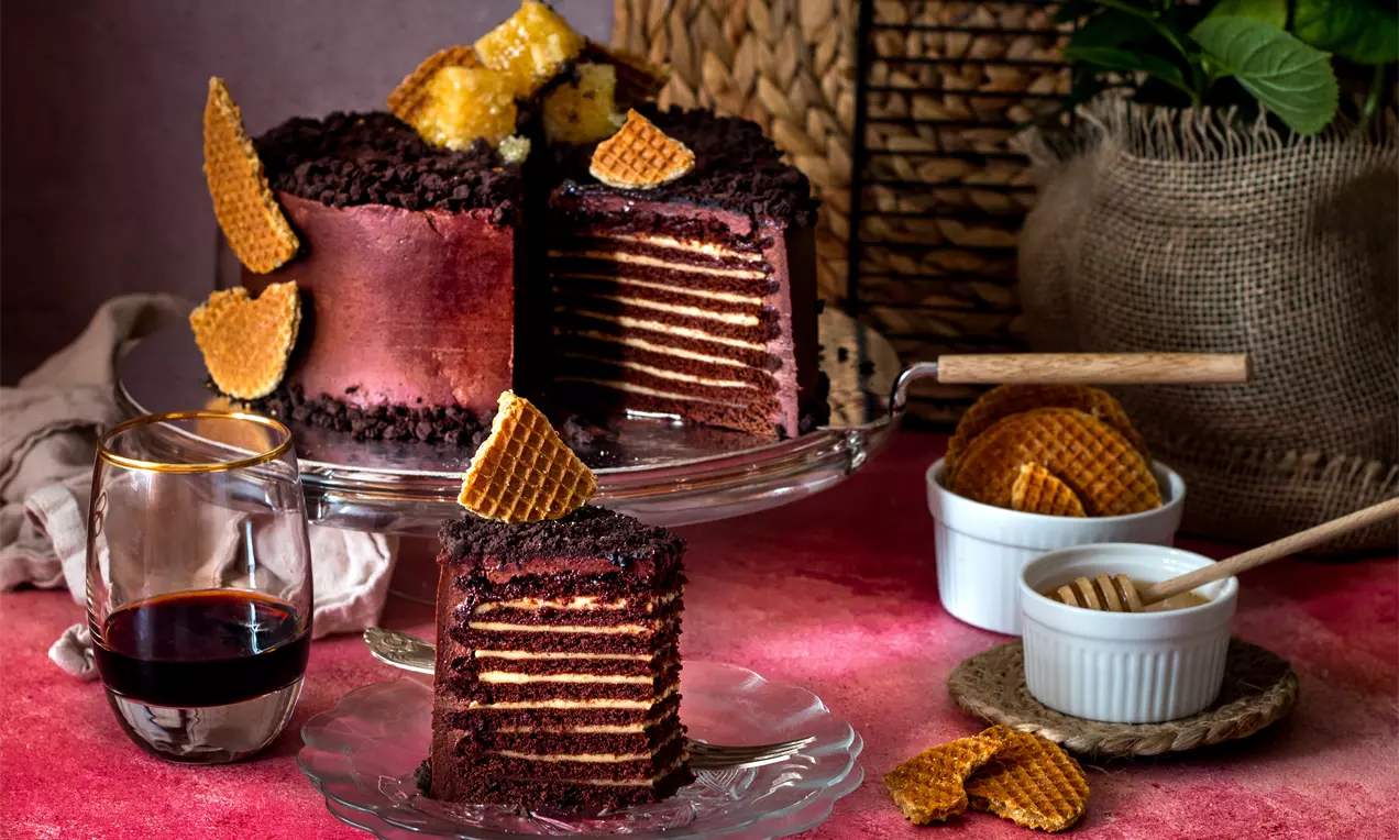 Шоколадово-медена торта с наситено кафяви шоколадови пластове и златисти медени корички, сервирана на стъклена подложка и стъклена чиния
