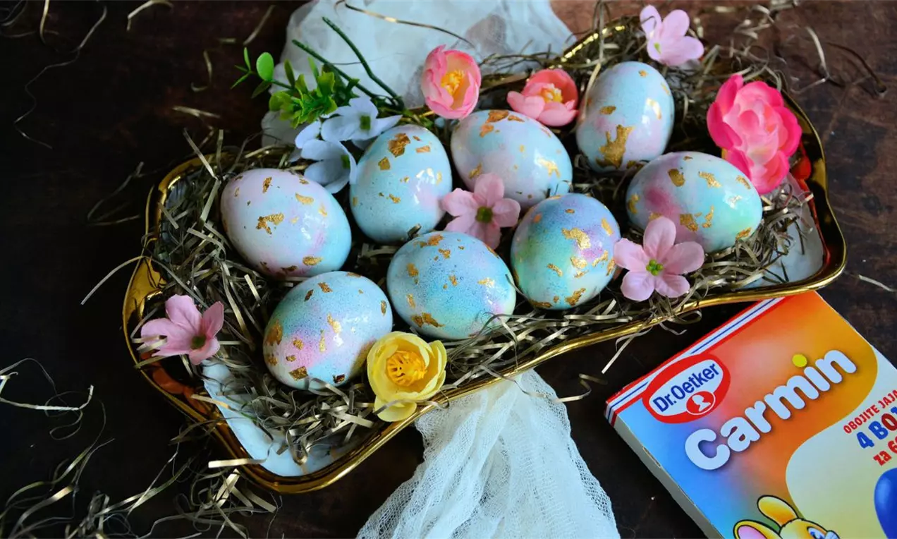 Uređena Vaskršnja jaja pastelnih nijansi ukrašena zlatnim detaljima na posteljici od prirodne slame sa cvećem i svetlim dekorom