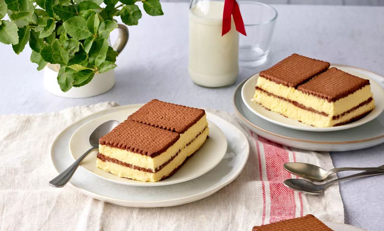 Butterkeks-Vanillecreme-Schnitten mit braunen Keksquadraten und gelber Creme, angerichtet auf weißen Tellern mit Metalllöffeln