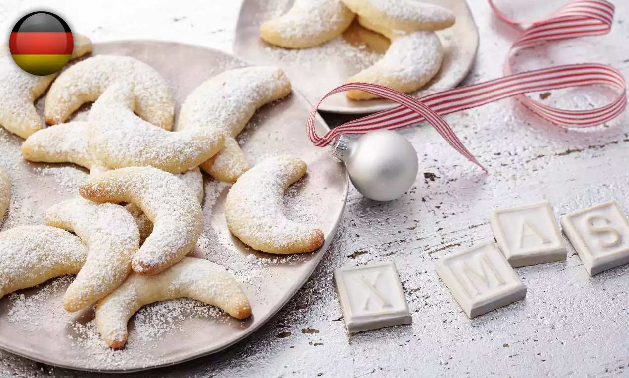 Fursecuri semilună aurii, fragede, presărate cu zahăr pudră alb, așezate pe o farfurie metalică împreună cu decorațiuni de sărbători