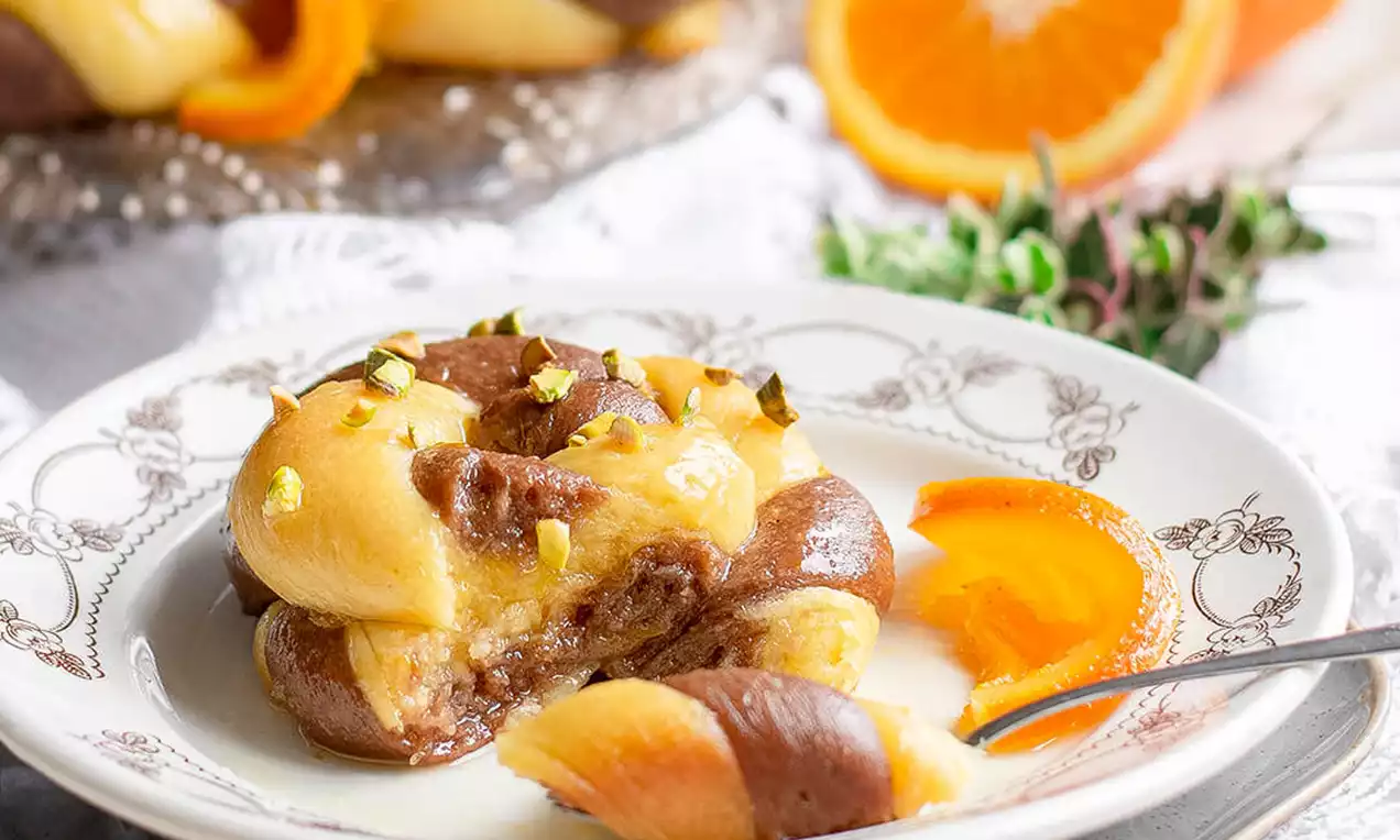 Turbani od svijetlog i tamnog tijesta spiralno oblikovani, mehki i sjajni, posuti sjeckanim pistacijama, servirani uz svježe kriške narandže