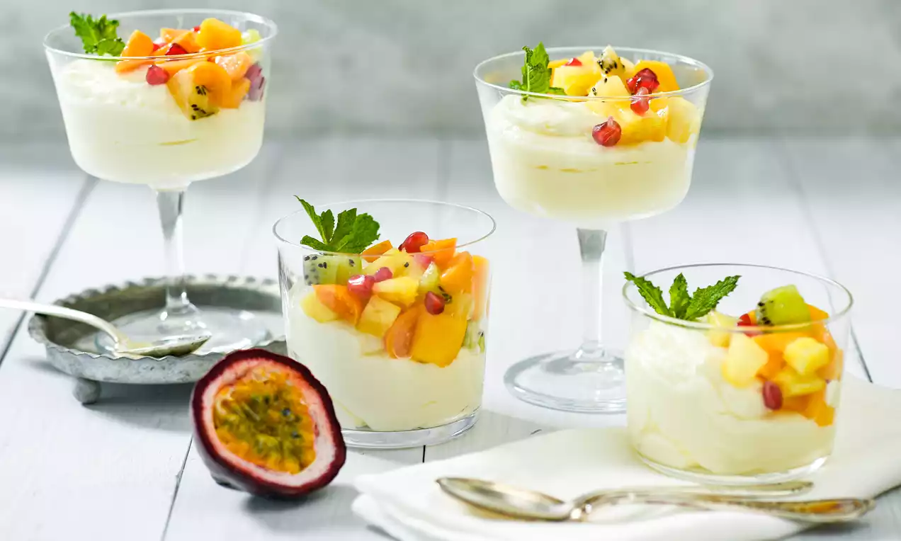 Joghurt-Dessert in transparenten Gläsern, bedeckt mit farbigem Obstsalat aus Mango, Kiwi und Granatapfel, garniert mit Minzblättchen