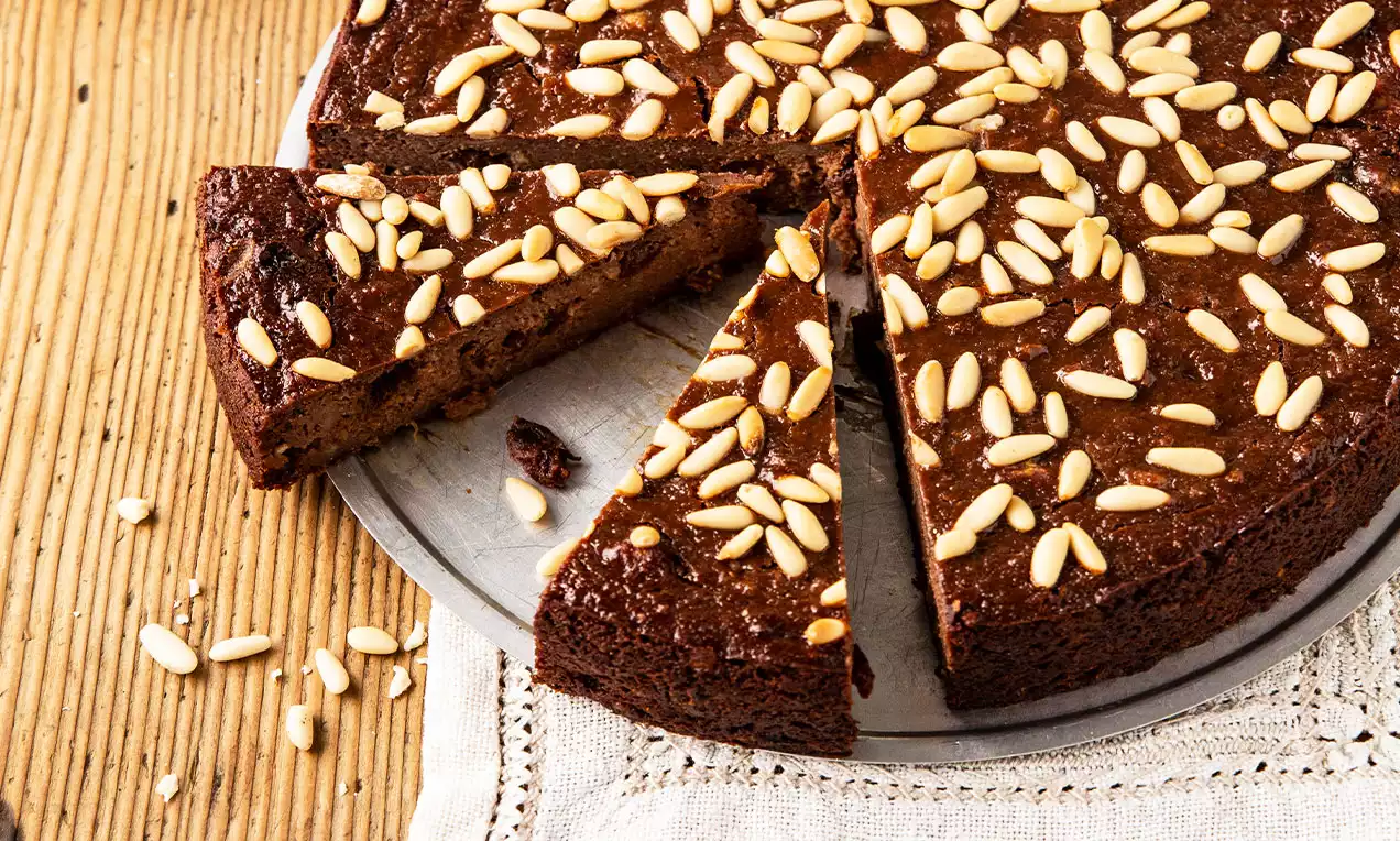 Tarte ronde brun doré aux textures denses avec des pignons de pin parsemés sur le dessus, présentée sur une assiette métallique