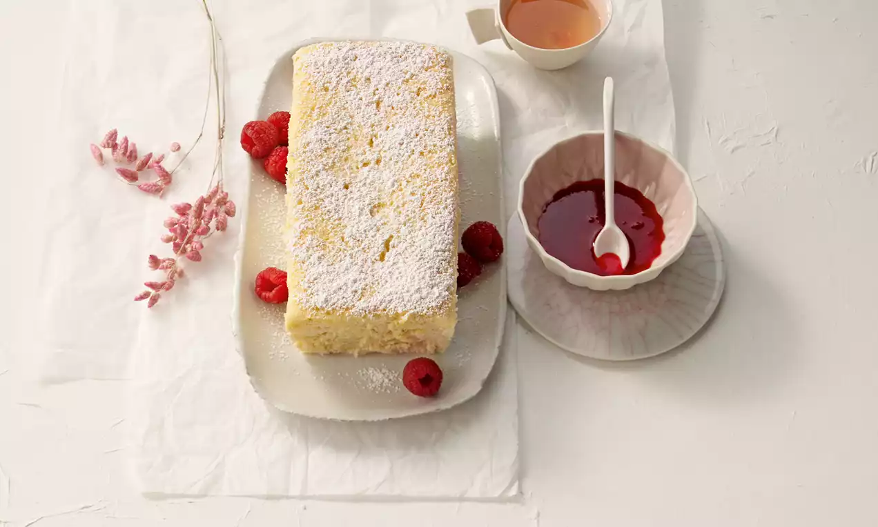 Japanischer Käsekuchen mit heller, lockerer Textur und Puderzucker bestäubt auf einem Teller mit frischen Himbeeren und Himbeersauce serviert