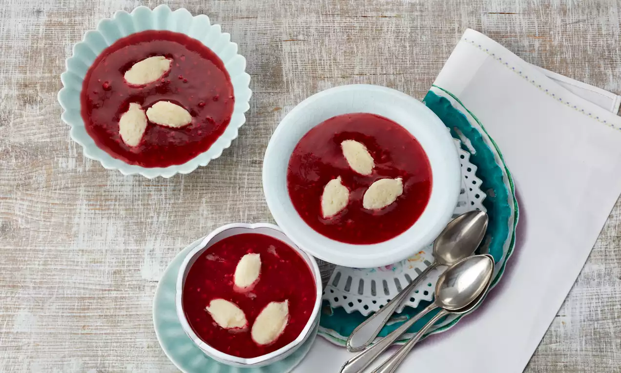 Kaltschale mit Grießklößchen in einer weißen Schale: rosarote Fruchtsuppe mit kleinen weißen Grießklößchen, Beeren und Minzblatt garniert