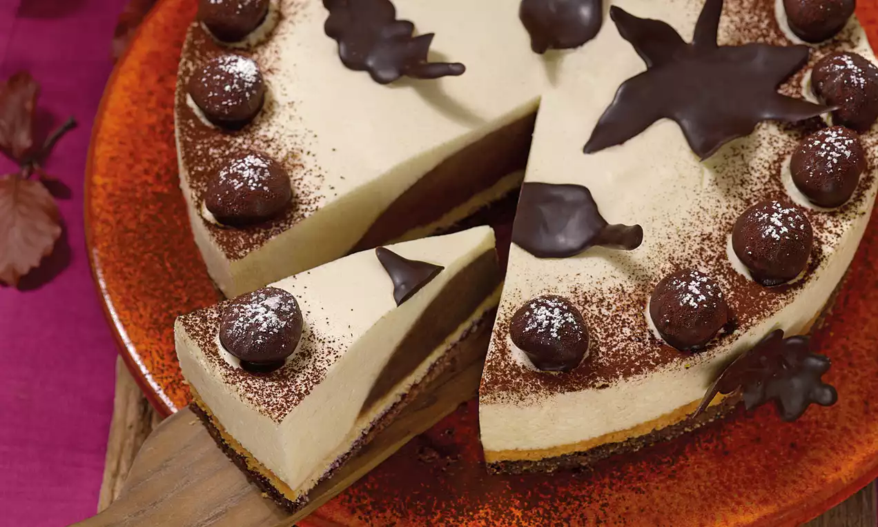 Maroni-Torte mit cremiger, beigefarbener Füllung, dunkler Schokoladenschicht, Schoko-Dekor und Kakao bestäubt auf rotem Teller