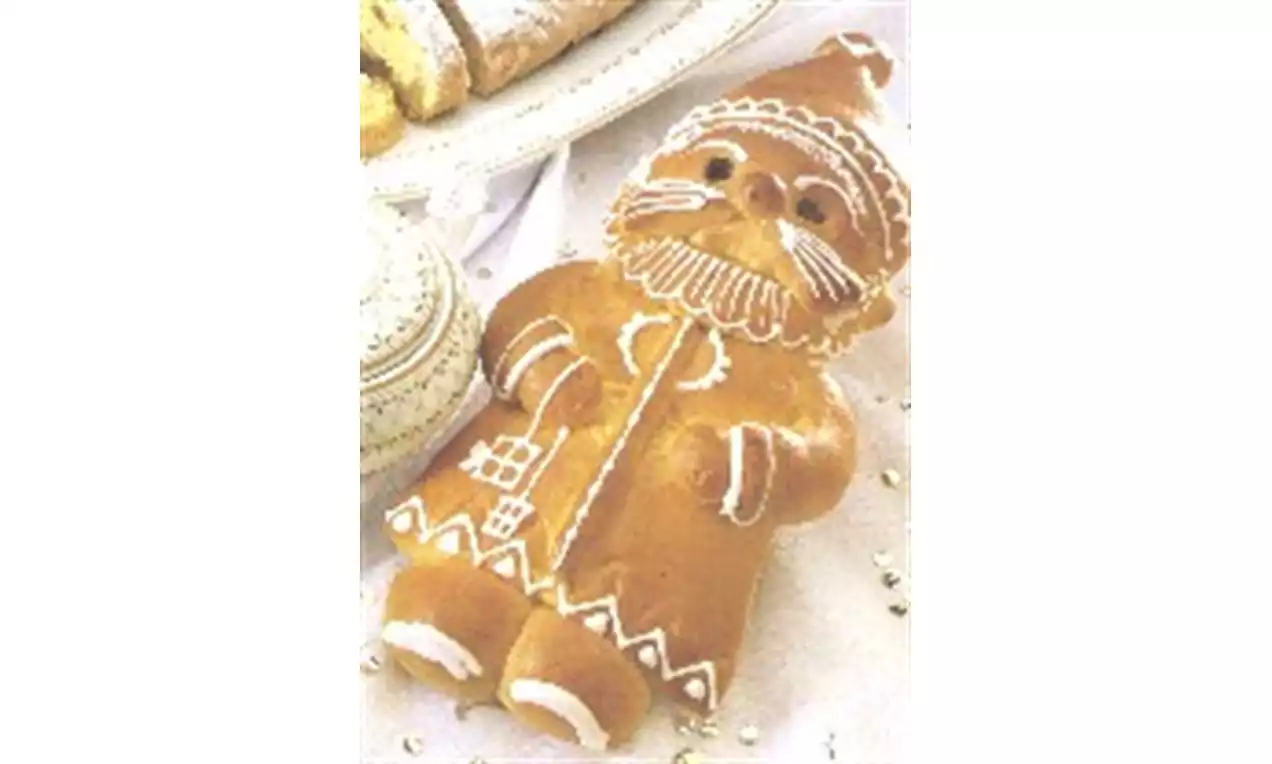 Goudbruine koek in de vorm van een kerstman met witte glazuurdetails voor baard, jas en laarzen op een wit bord met kerstgebak