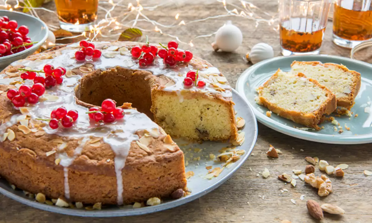 Cake doré en couronne avec glaçage blanc, éclats d’amandes et groseilles rouges, trous de partages sur assiette grise