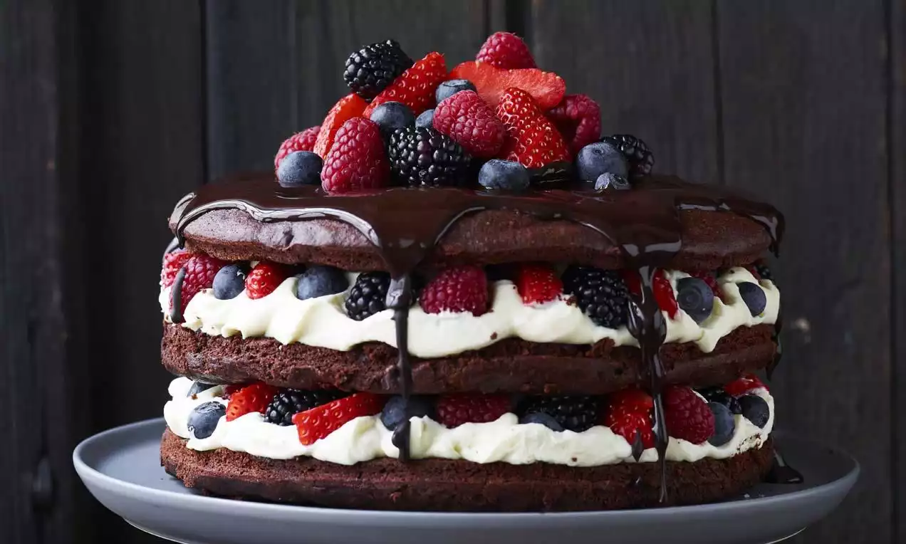 Saftig sjokoladekake i to lag med hvit sjokolademousse, mørk glasur og toppet med ferske bær på et mørkt kakefat