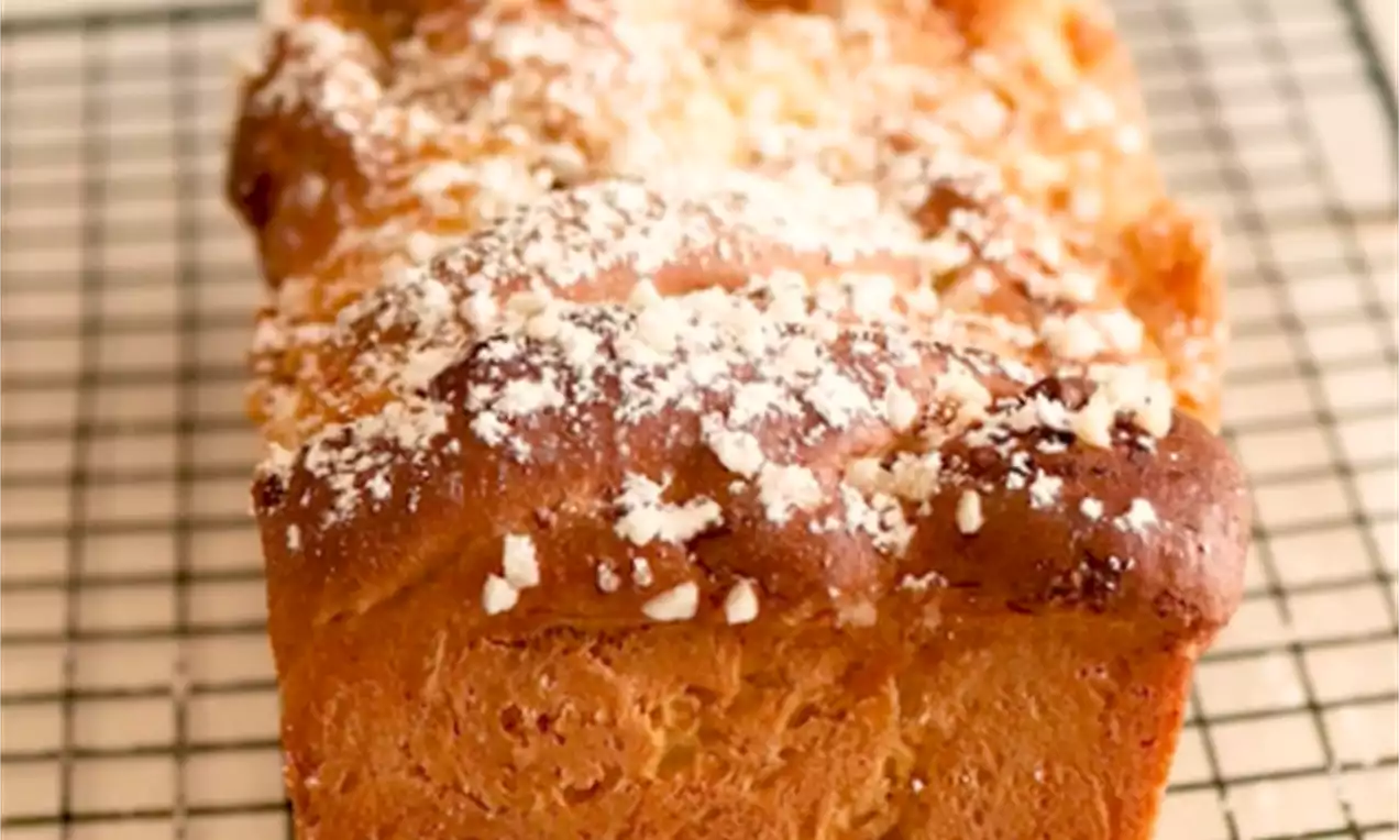 Babka u obliku zlatnosmeđeg kvadra s nepravilnim, valovitim vrhom, posuta krupnim bijelim šećerom, na metalnoj rešetki za hlađenje