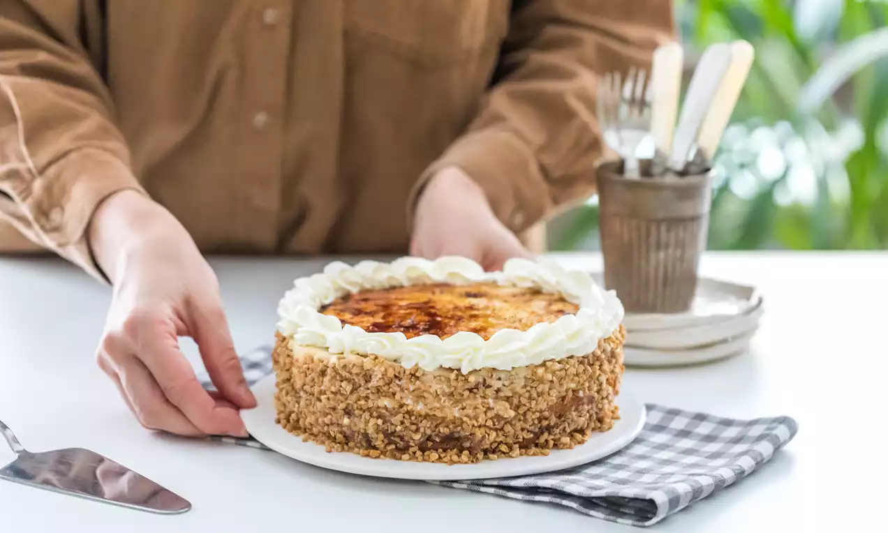 Tarta redonda con cobertura brillante de yema caramelizada, borde de nata en rosetones y laterales cubiertos con almendra picada