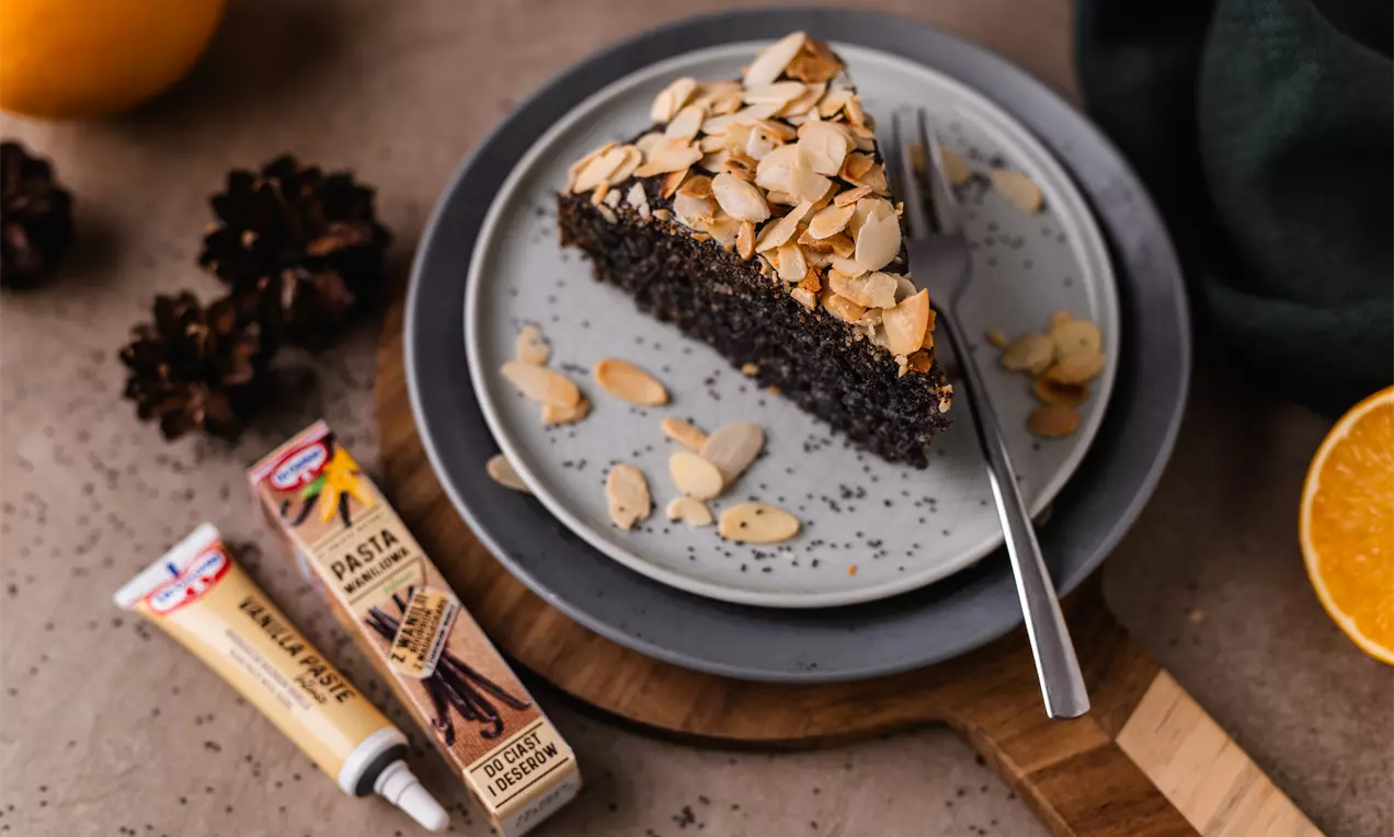 Trapus ir drėgnas migdolinis pyragas sodriai rudos spalvos, papuoštas skrudintais migdolų griežinėliais, patiektas ant šviesiai pilkos lėkštės